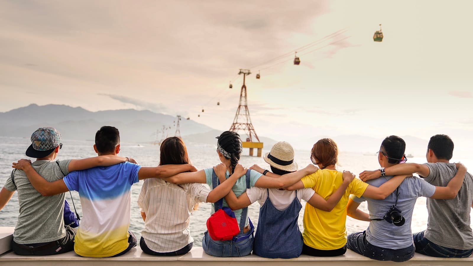 Friends sitting together by the water, looking toward mountains and cable cars.